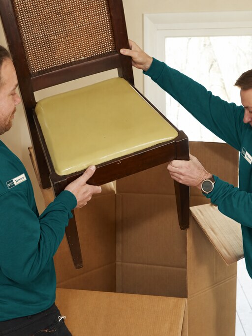 Two movers carefully placing a chair into a protective moving box